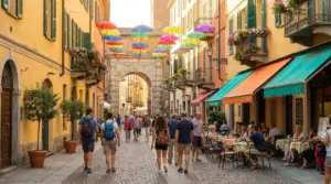 Persone passeggiano in una via pedonale con ombrelli colorati sospesi e caffè all'aperto
